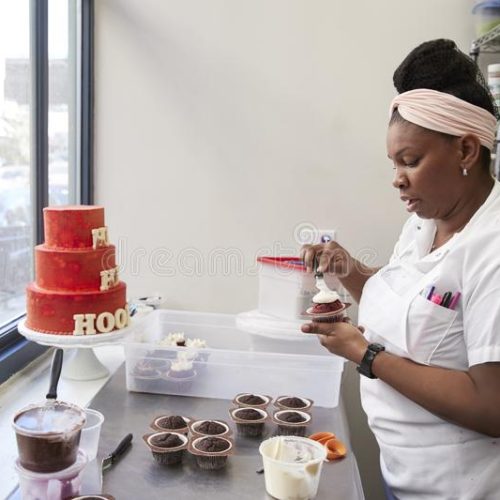 young-black-woman-frosting-cakes-bakery-108977274